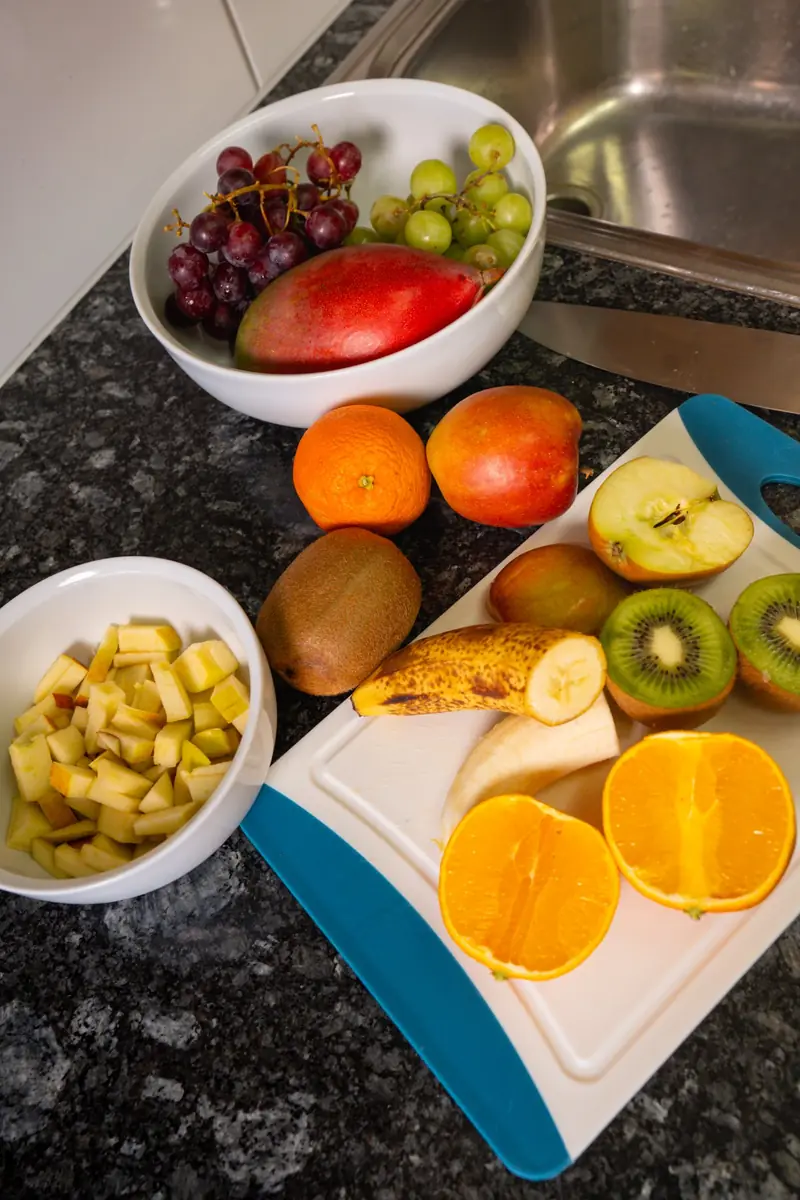 Früchte auf einer Küchenablage: Trauben, Mango, Kiwi, Orangen und eine Schale mit gewürfelten Äpfeln