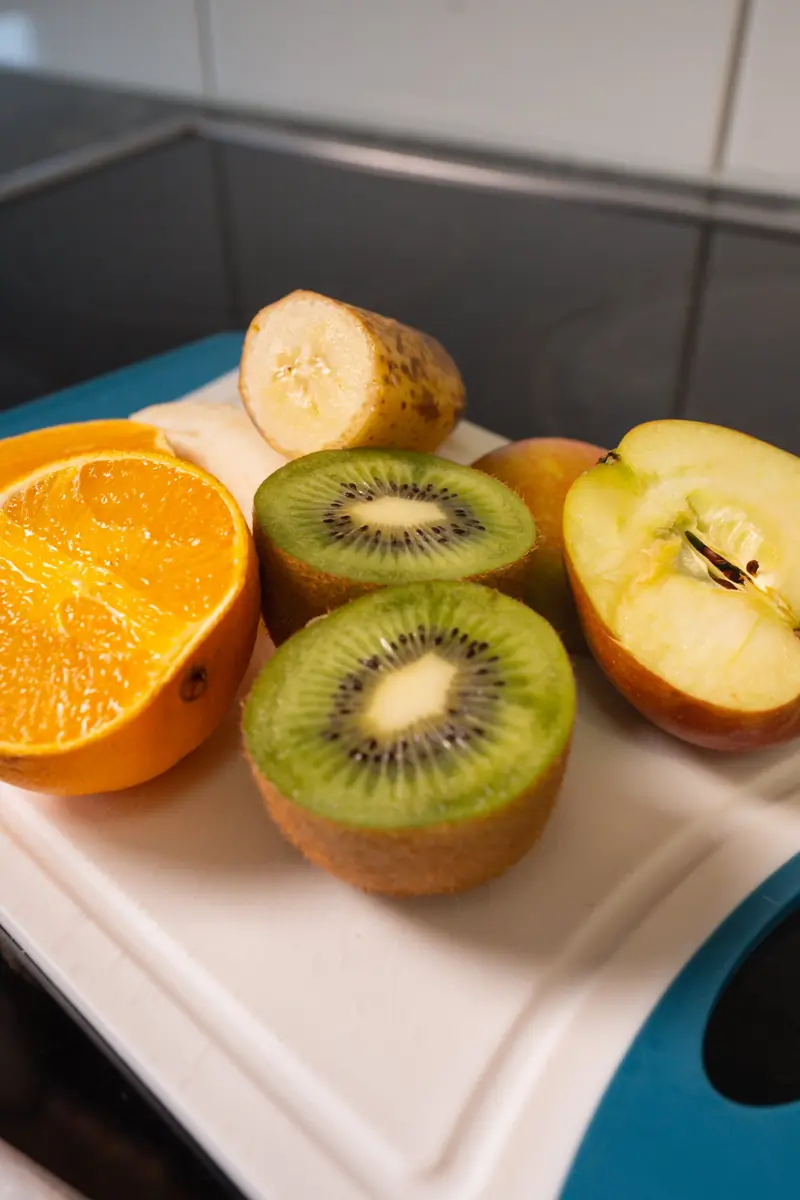 Aufgeschnittene Orange, zwei Kiwihälften, ein halber Apfel und eine Banane auf einem Schneidebrett