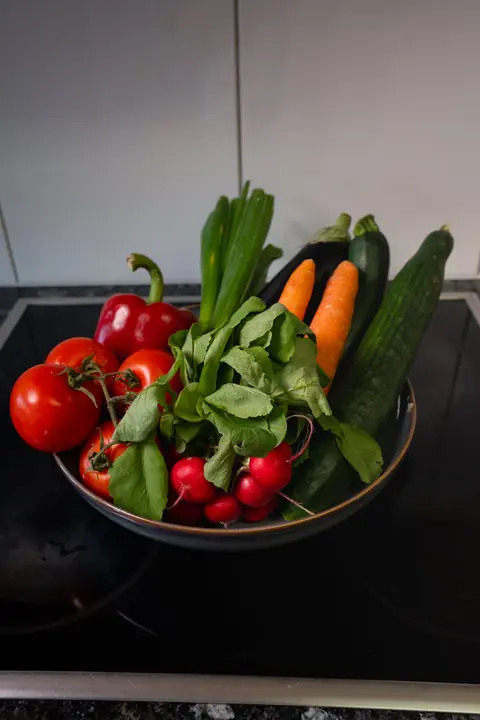 Schale mit Tomaten, Peperoni, Radieschen, Rüebli, Zucchetti und Gurke auf einem schwarzen Kochfeld