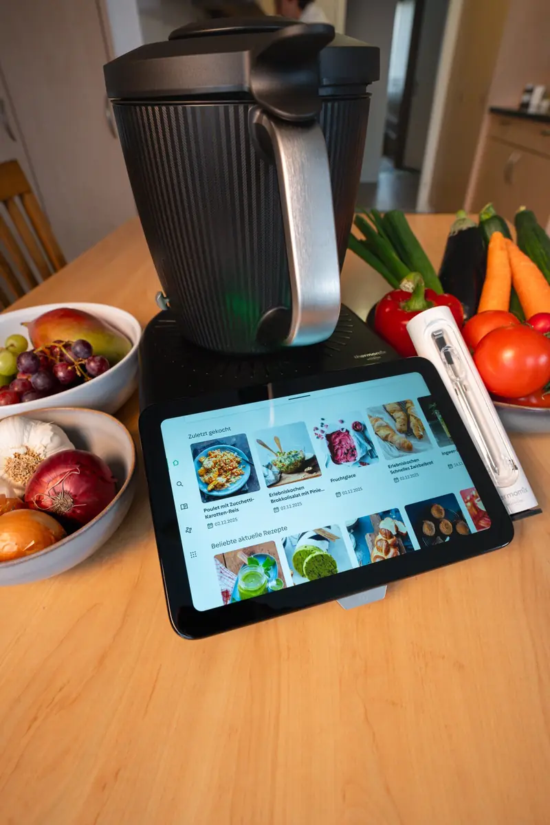 Thermomix mit Tablet auf einem Holztisch, umgeben von Gemüse und Schalen, bereit für einen Kochkurs